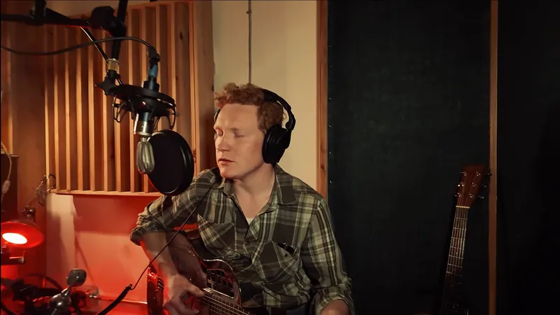 Singing into a studio microphone, resonator guitar in hand